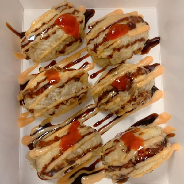 Six deep-fried sushi rolls drizzled with dark and light sauces, topped with red sriracha.