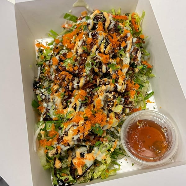 Ryuu Bowl's Japanese salad with lettuce, sauces, green onions, and orange tobiko in a white box.