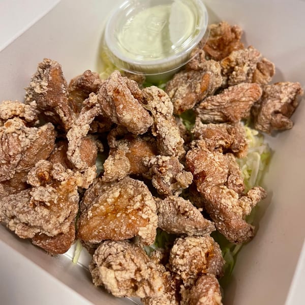 Crispy Japanese karaage chicken pieces with a side of green dipping sauce in a white container.